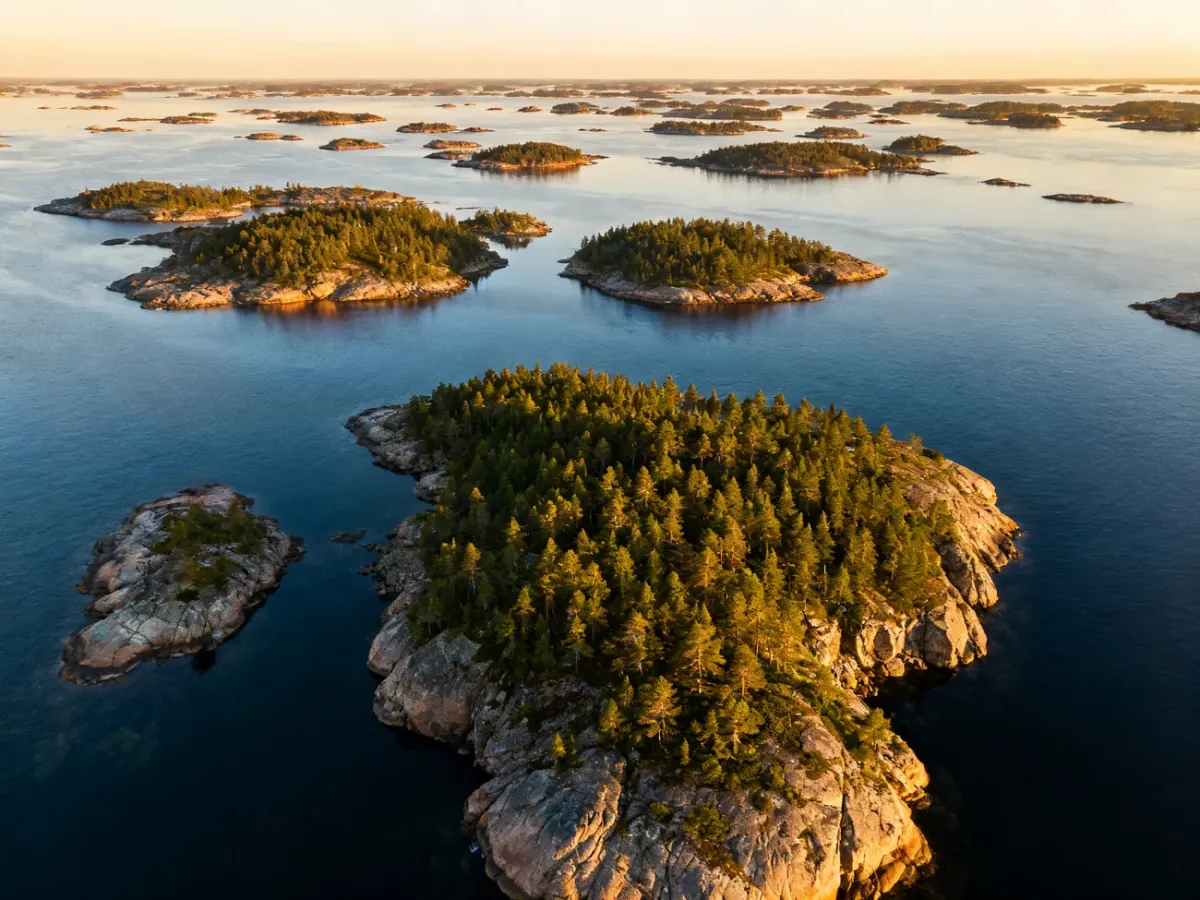 Widok z lotu ptaka na liczne skaliste wyspy i sosnowe lasy archipelagu w Skandynawii o zachodzie słońca.